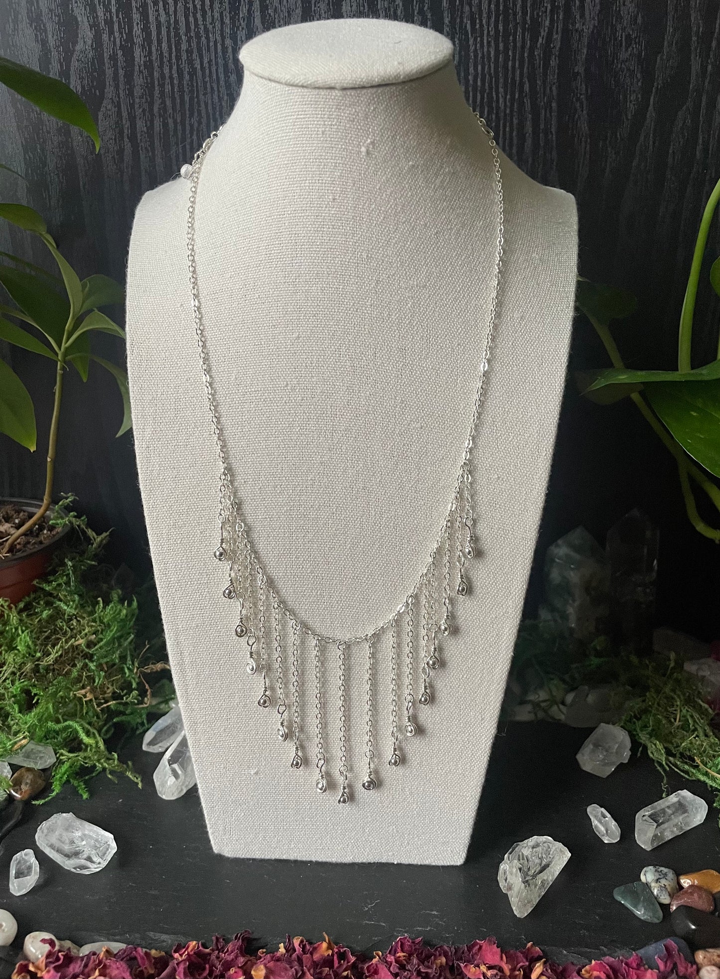 Silver necklace on a white bust with a dark background and decorative elements.