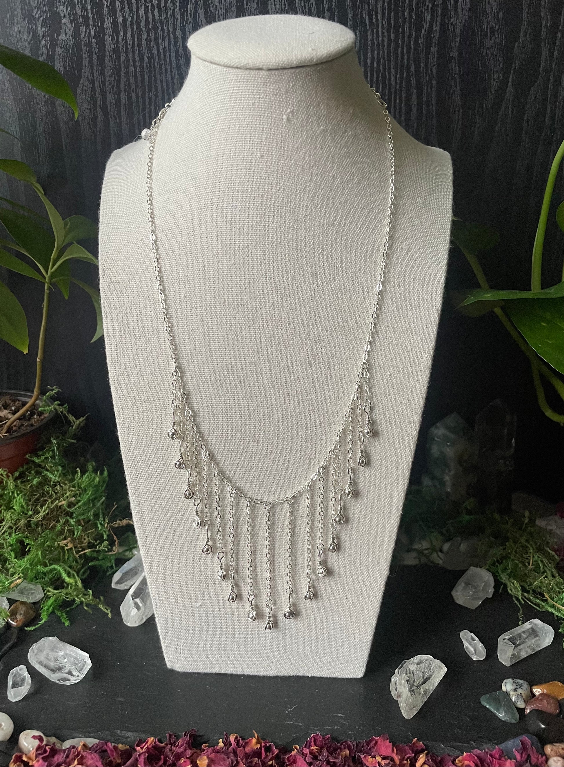 Silver necklace on a white bust with a dark background and decorative elements.