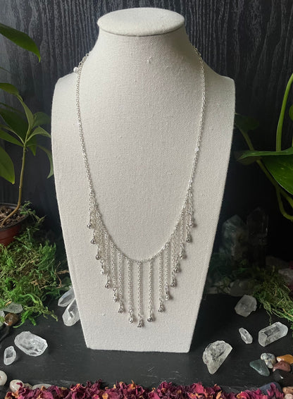 Silver necklace on a white bust with a dark background and decorative elements.