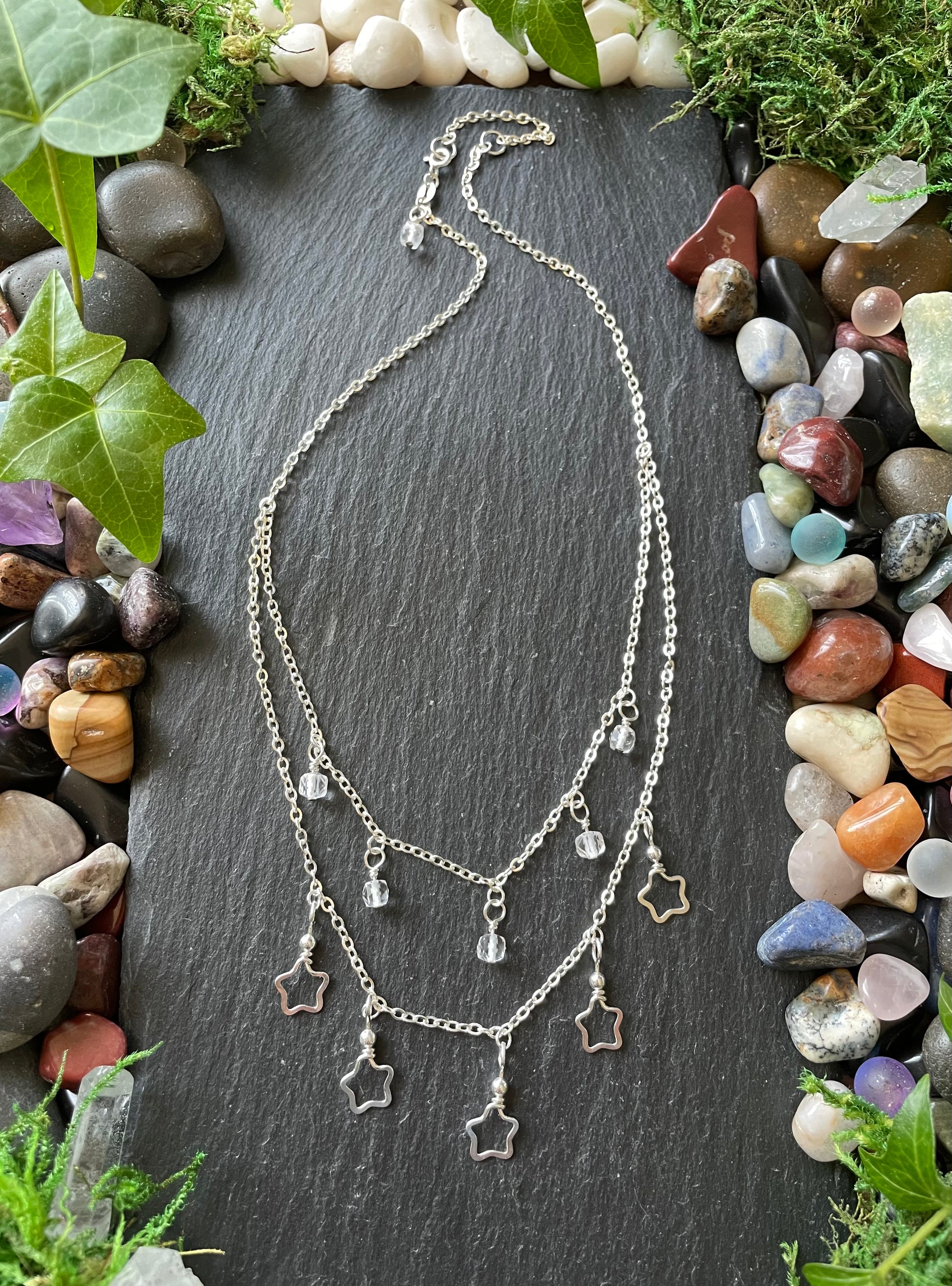 Necklace with star-shaped charms on a dark slate surface surrounded by stones and plants