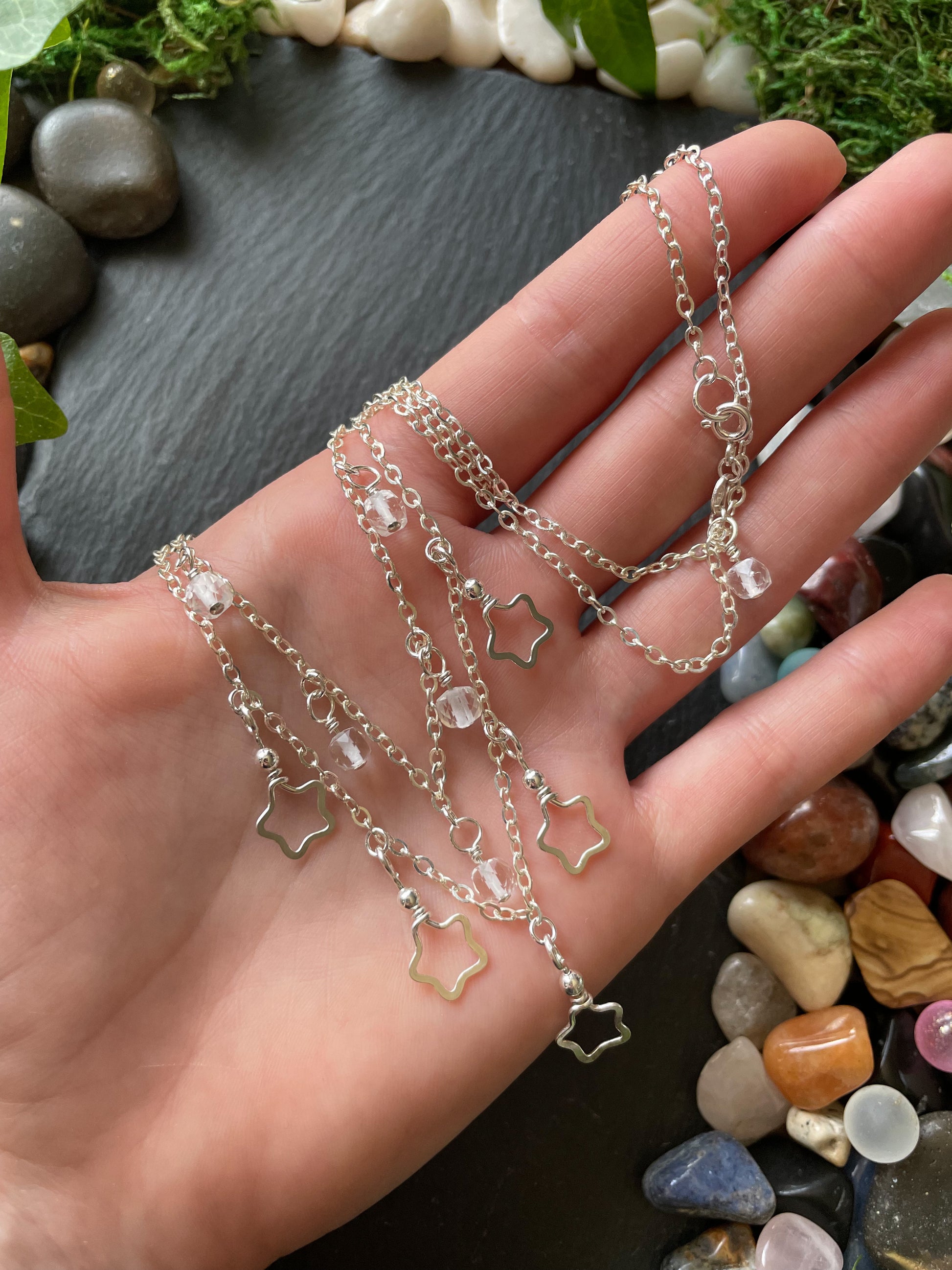 Hand holding layered silver chain necklace with star charms on a natural stone background