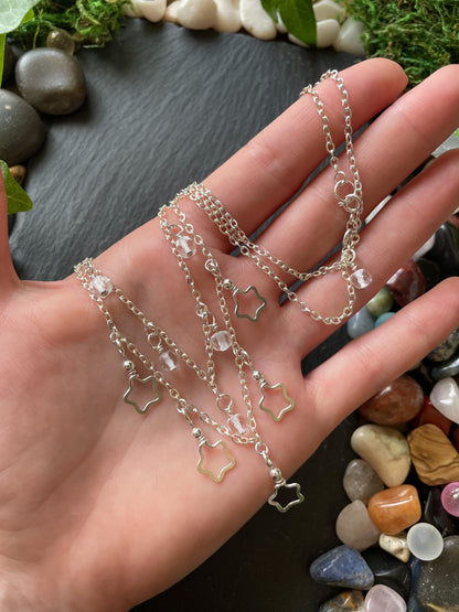 Hand holding layered silver chain necklace with star charms on a natural stone background