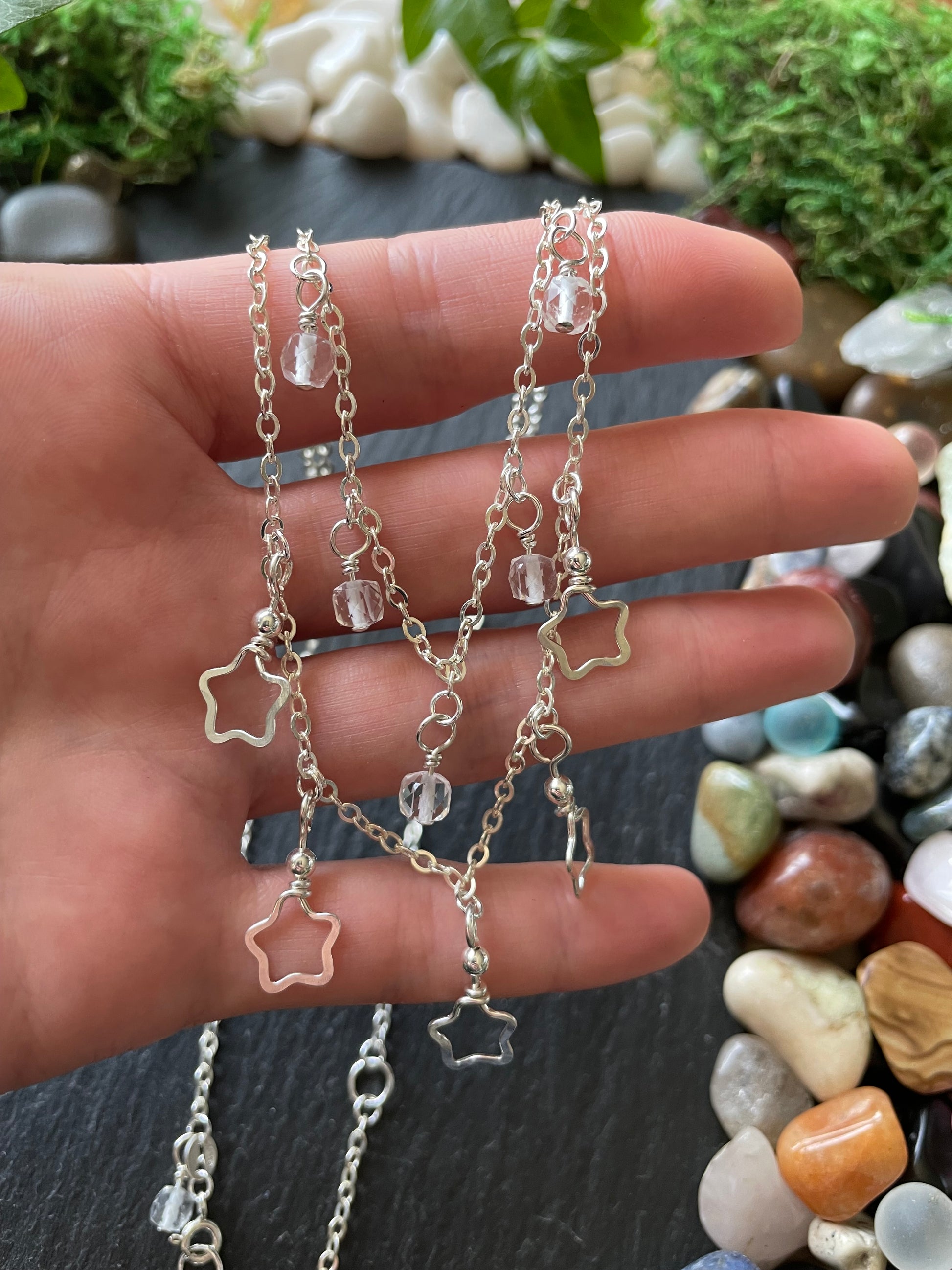 Hand holding layered star charm necklace with a natural stone background