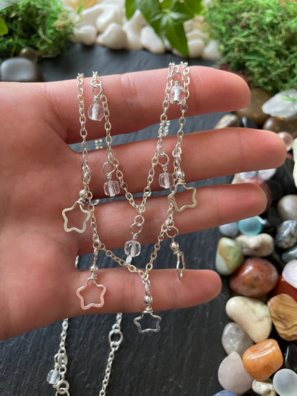 Hand holding layered star charm necklace with a natural stone background