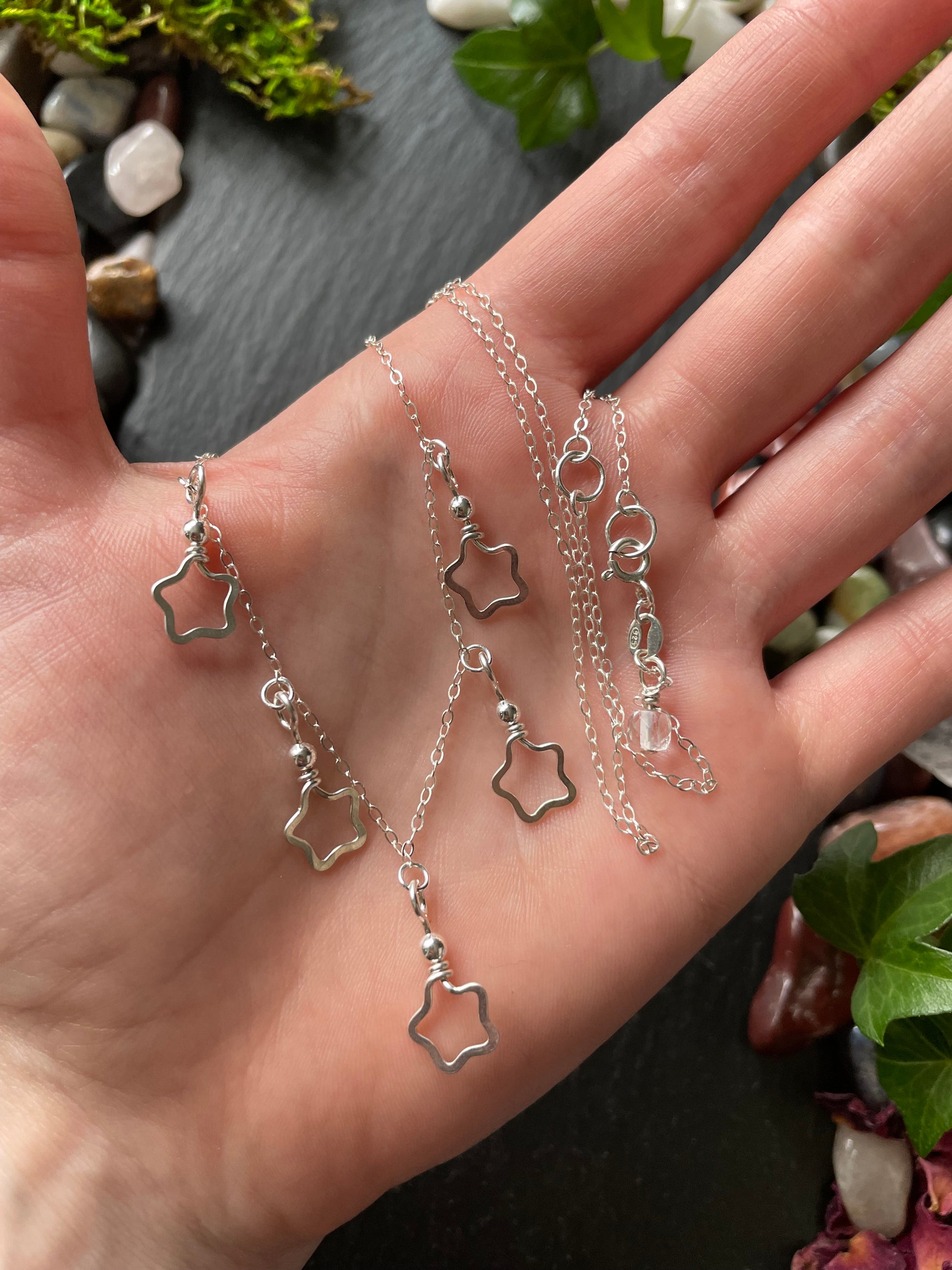 Hand holding delicate silver star charm necklace on a natural background