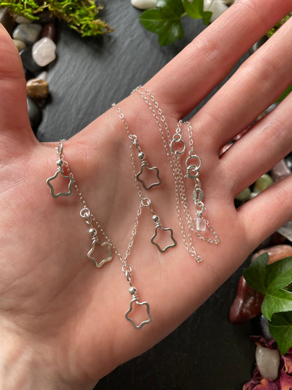 Hand holding delicate silver star charm necklace on a natural background