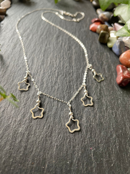 Delicate silver star charm necklace on a dark stone surface with pebbles in the background