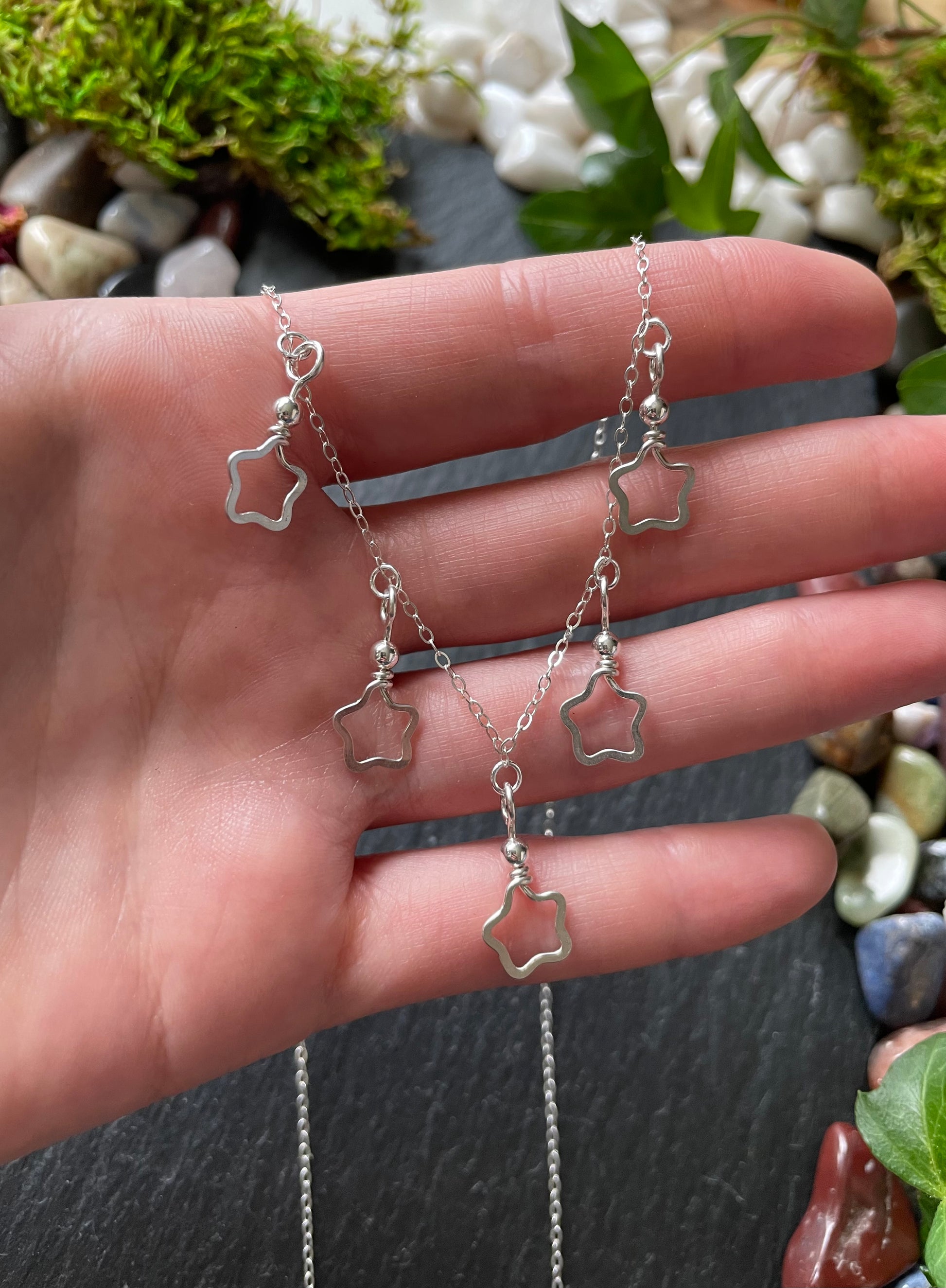 Silver star-shaped necklace held in a hand with a natural background