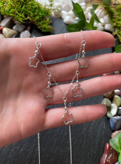 Silver star-shaped necklace held in a hand with a natural background