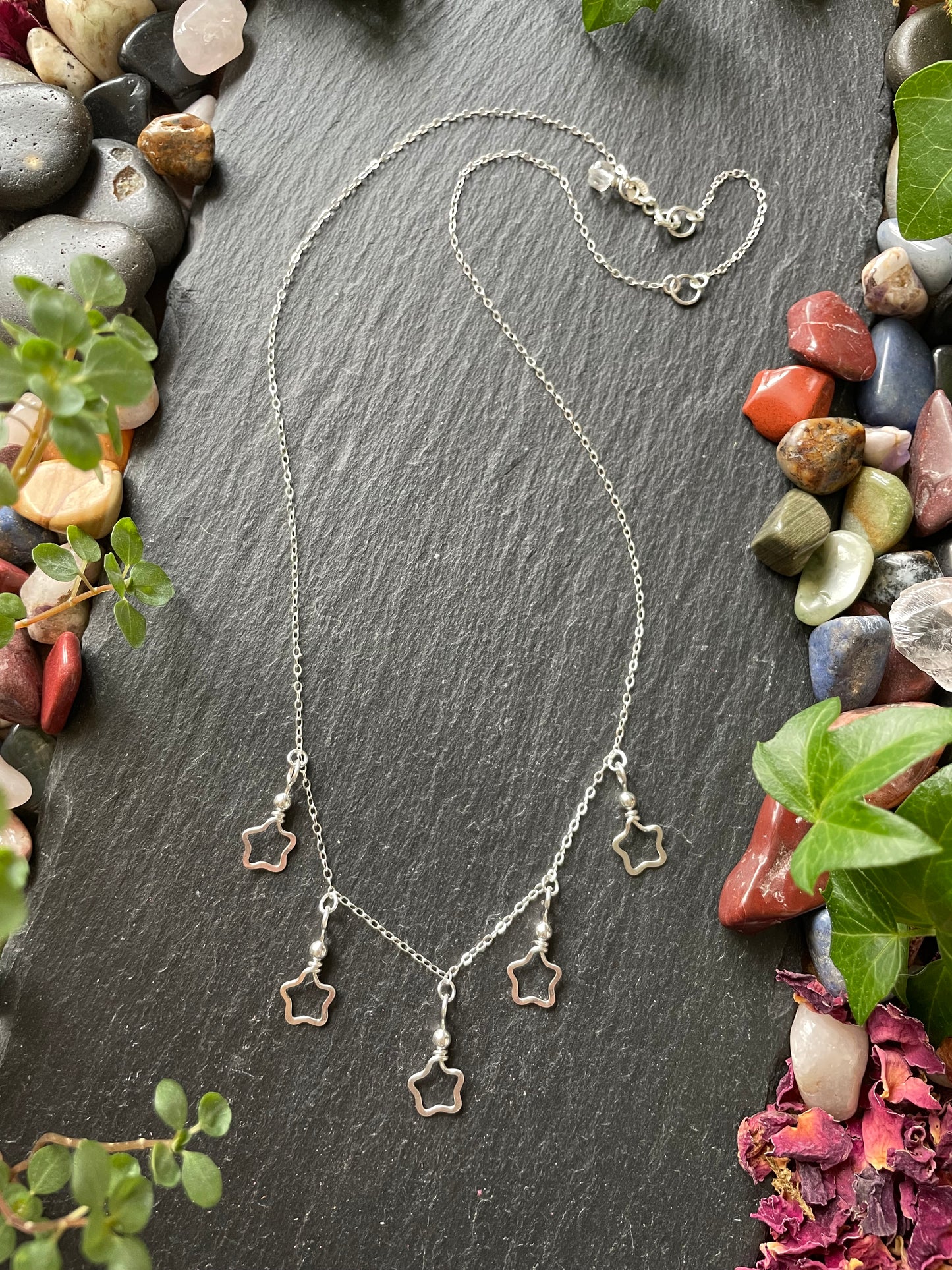 Silver necklace with star charms on a slate surface with stones and plants.
