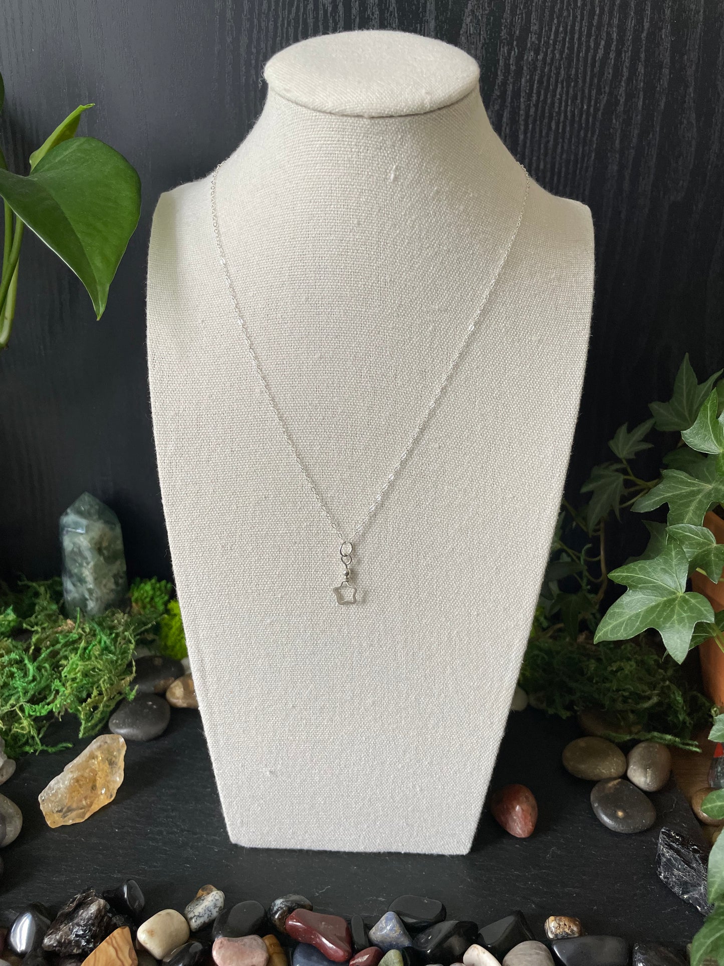 Silver star necklace on a white mannequin bust with a natural stone and plant background
