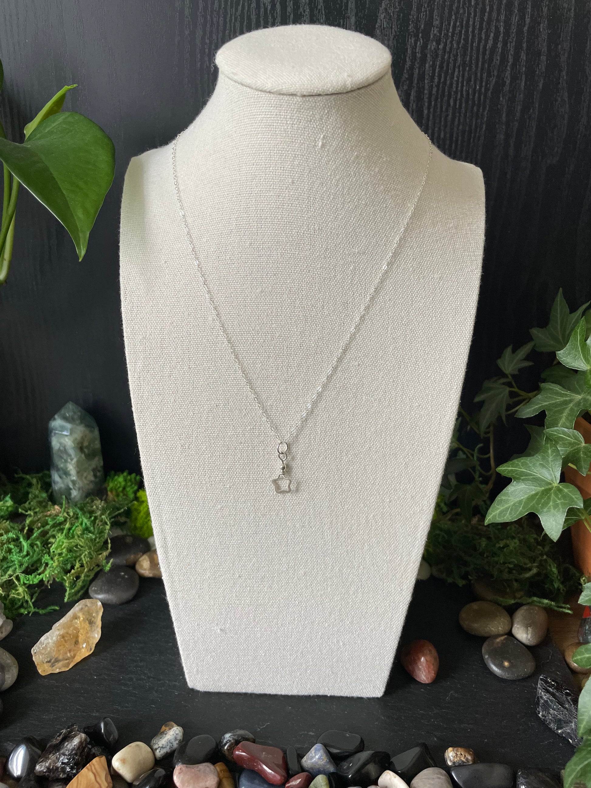 Silver star necklace on a white mannequin bust with a natural stone and plant background