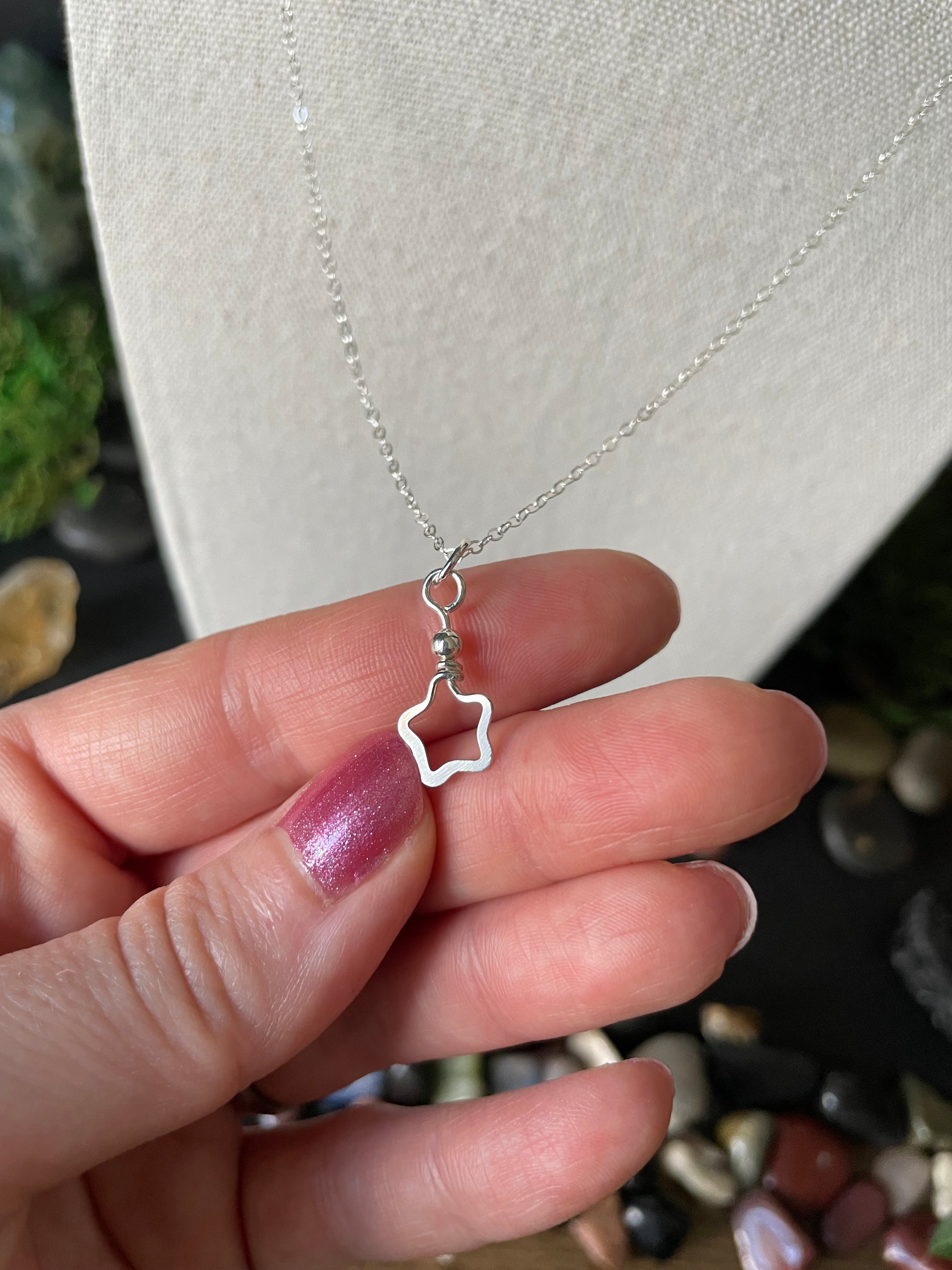 Hand holding a silver necklace with a star-shaped pendant against a blurred background