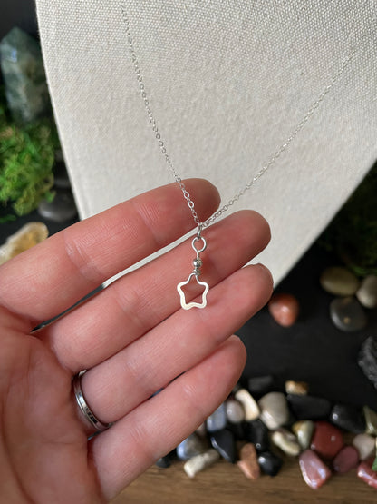 Silver star-shaped necklace being held by a hand against a background of colorful gemstones