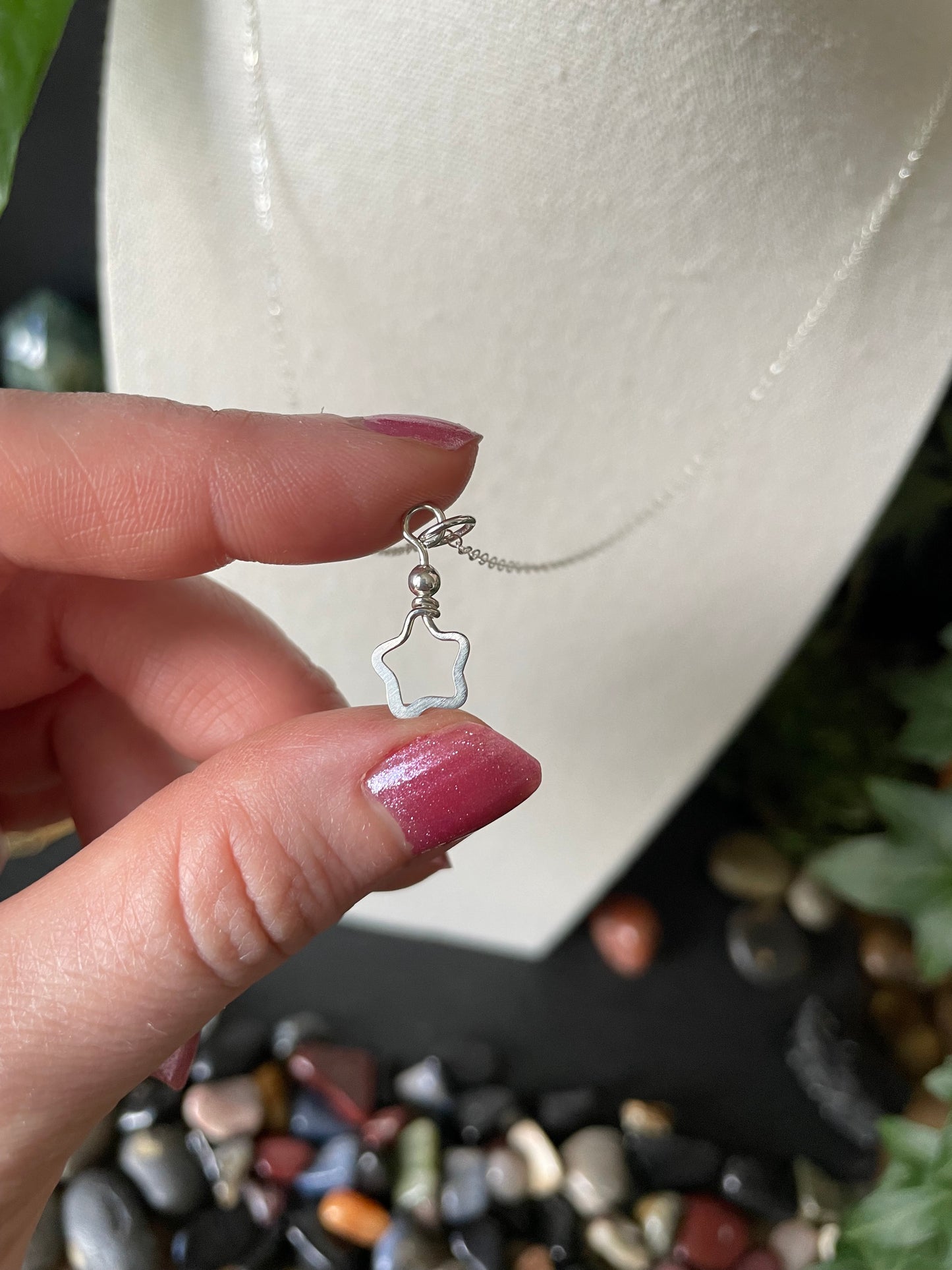Hand holding a necklace with a star-shaped pendant against a blurred background of stones and plants.