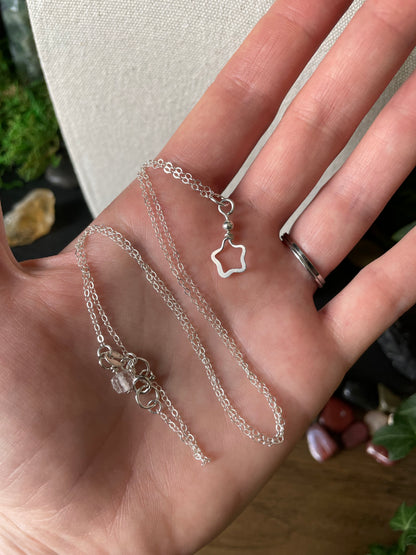 Hand holding a silver necklace with a star charm on a background with colorful gemstones