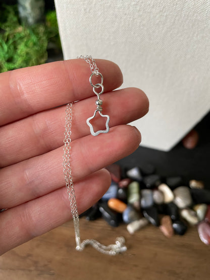 Silver necklace with a star shaped pendant held in hand, with a colorful gemstones background