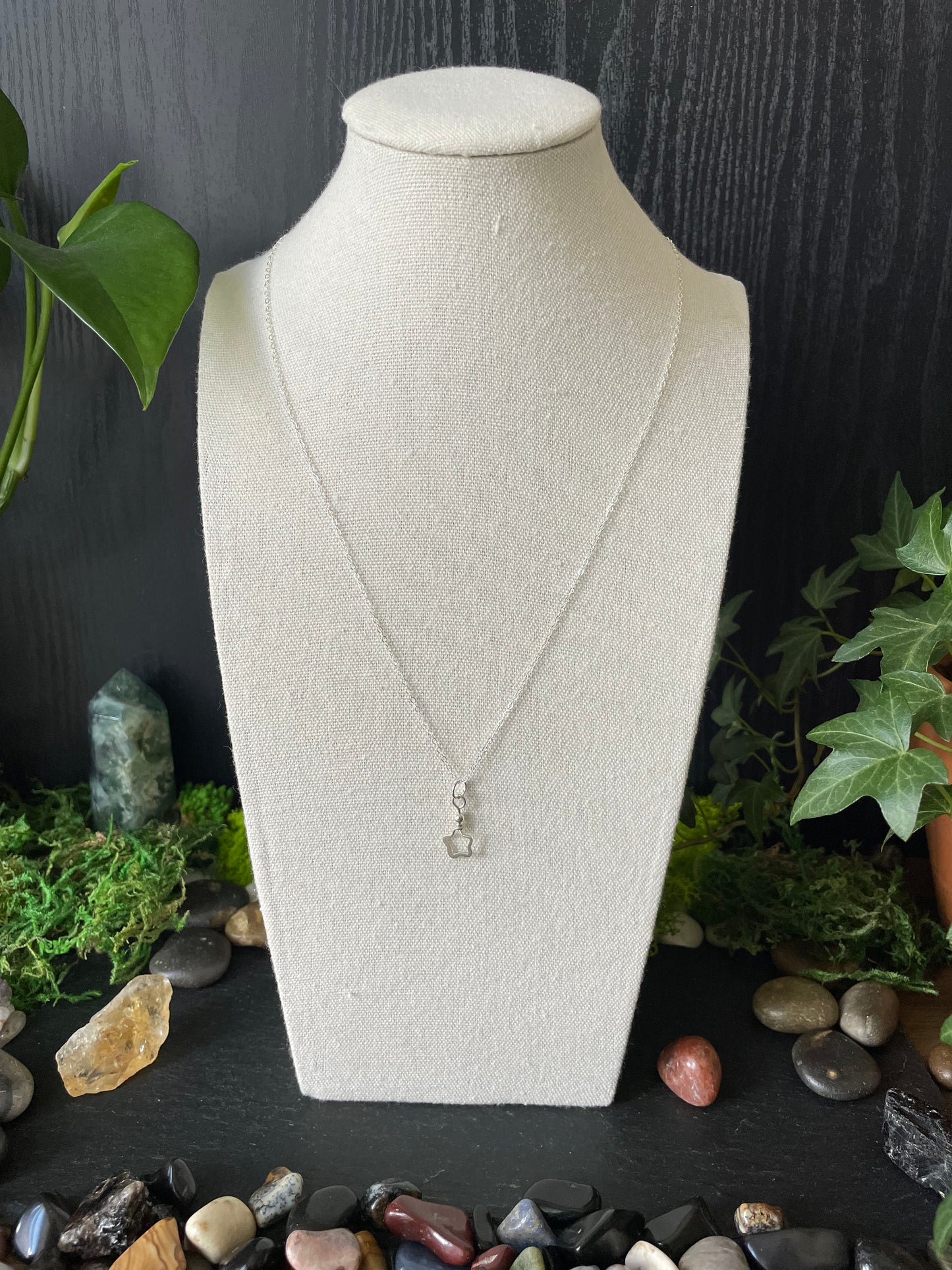 Dainty silver star necklace on a mannequin bust with a natural stone and plant background