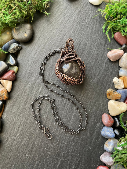 Necklace with a stone amulet on a dark surface surrounded by stones and moss