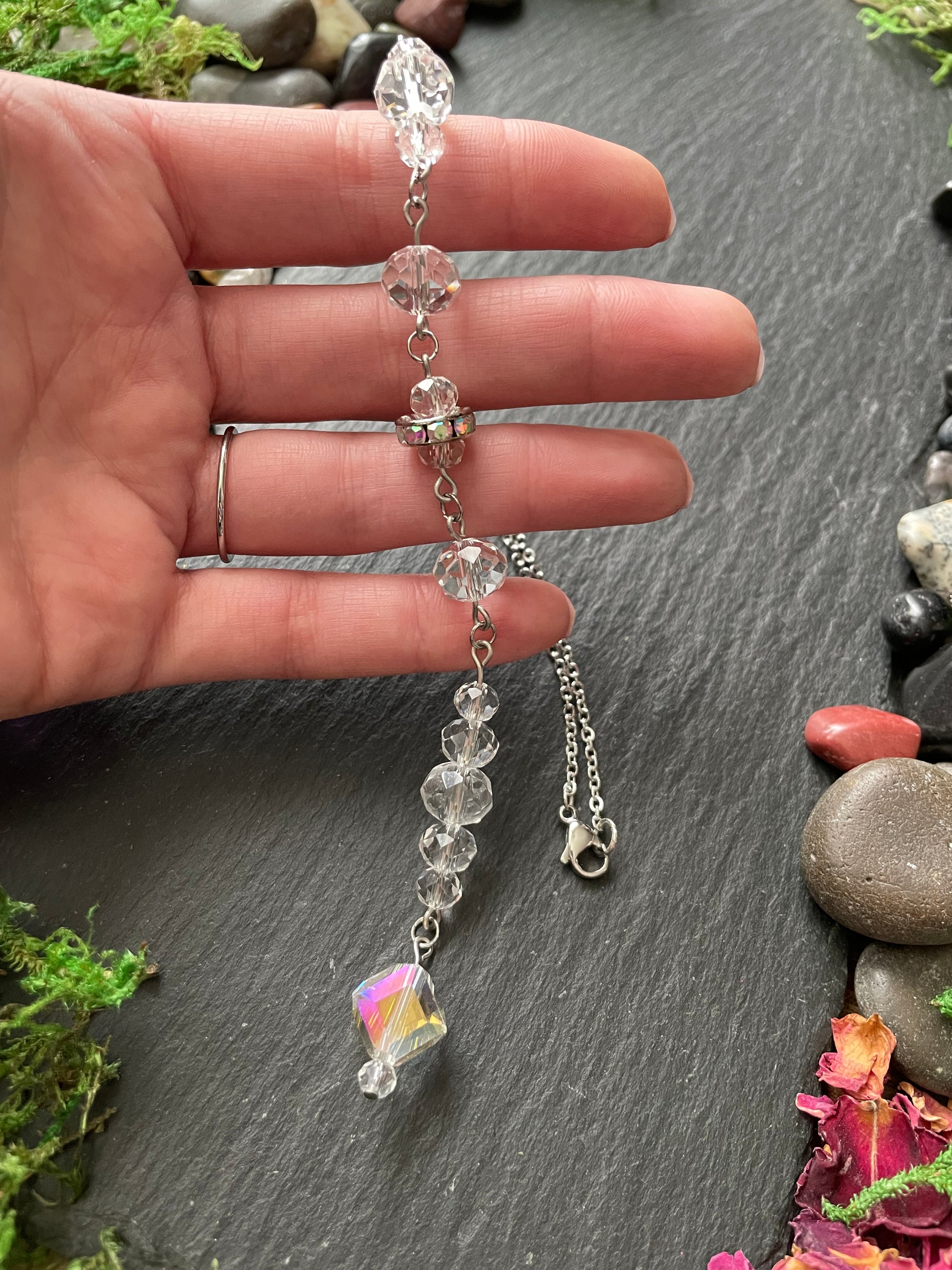 Hand holding a car mirror charm with clear beads on a natural stone background