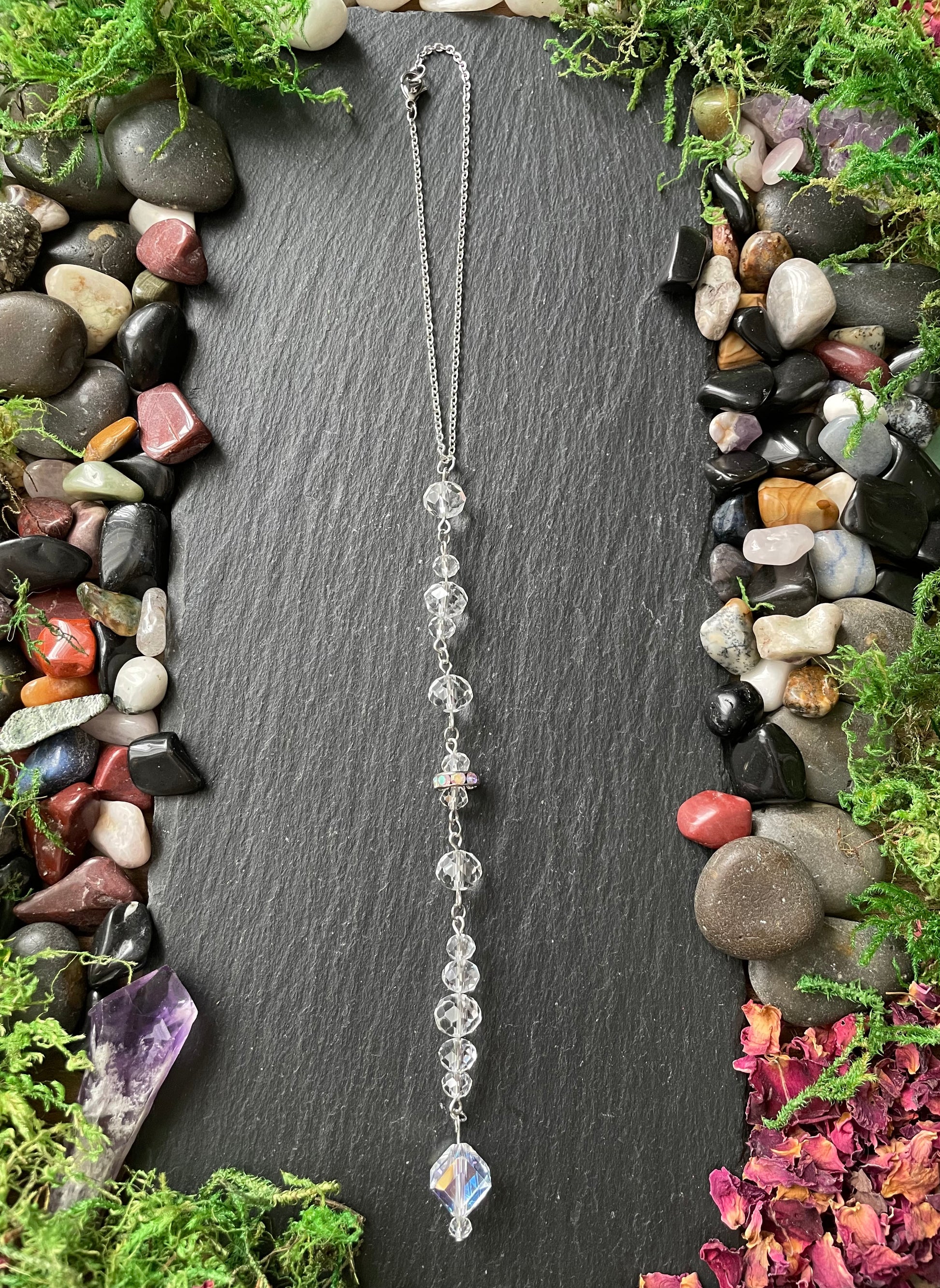 Car mirror charm with sparkly clear beads on a dark slate surface surrounded by gemstones and plants