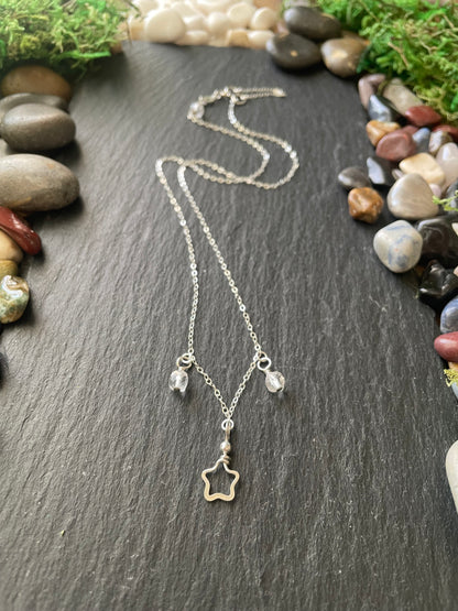 Silver necklace with star and bead charms on a dark surface with stones and moss.