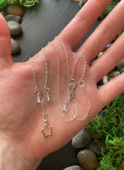 Hand holding a silver necklace with star  against a natural background.