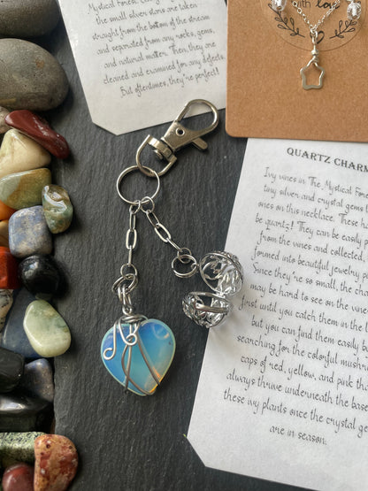 Silver keychain with a blue stone pendant on a slate surface with stones and text.