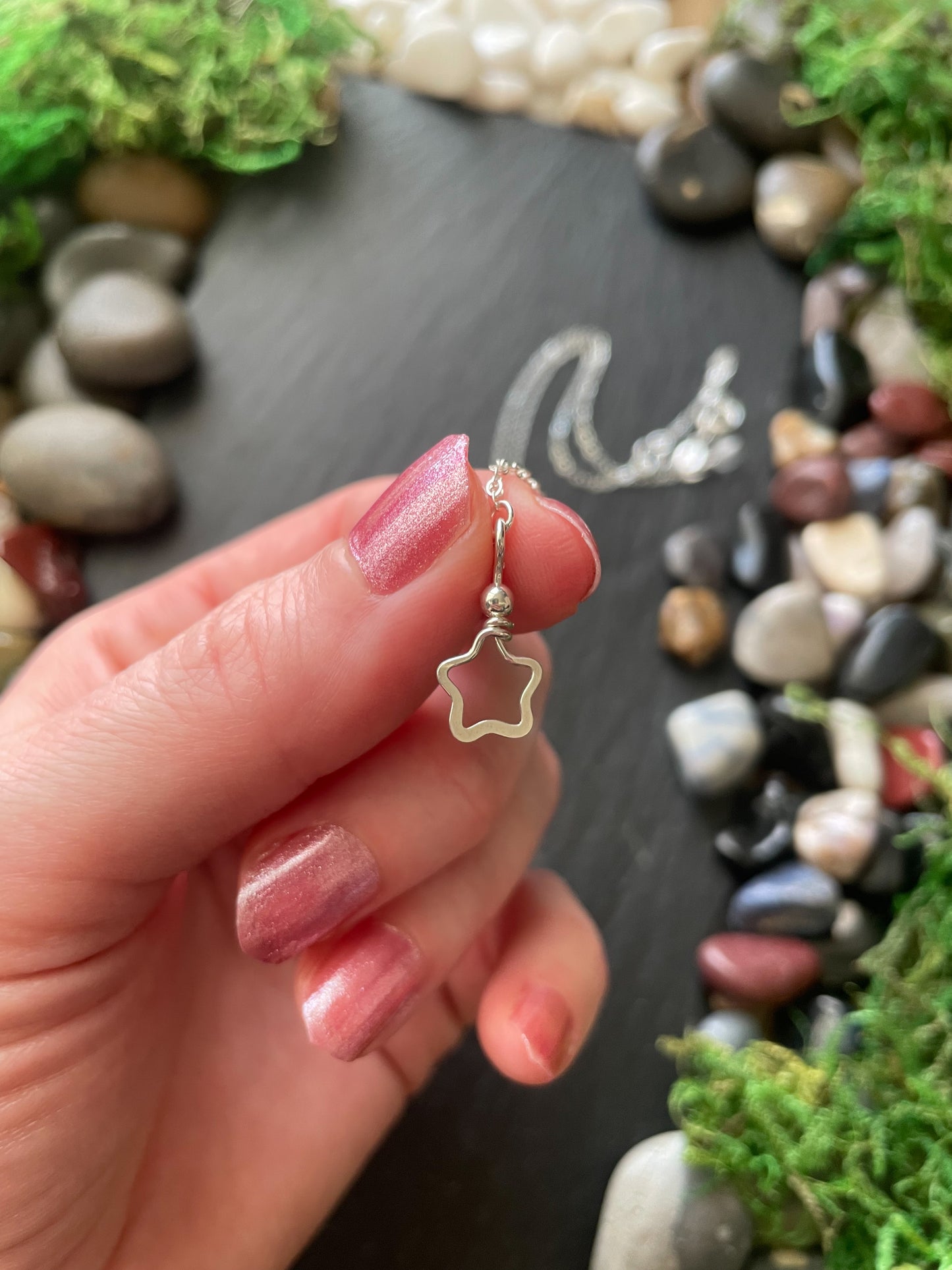 Hand holding a silver star-shaped pendant with a natural stone background