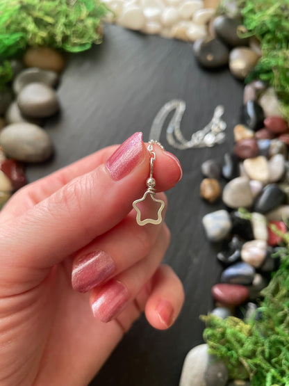 Hand holding a silver star-shaped pendant with a natural stone background