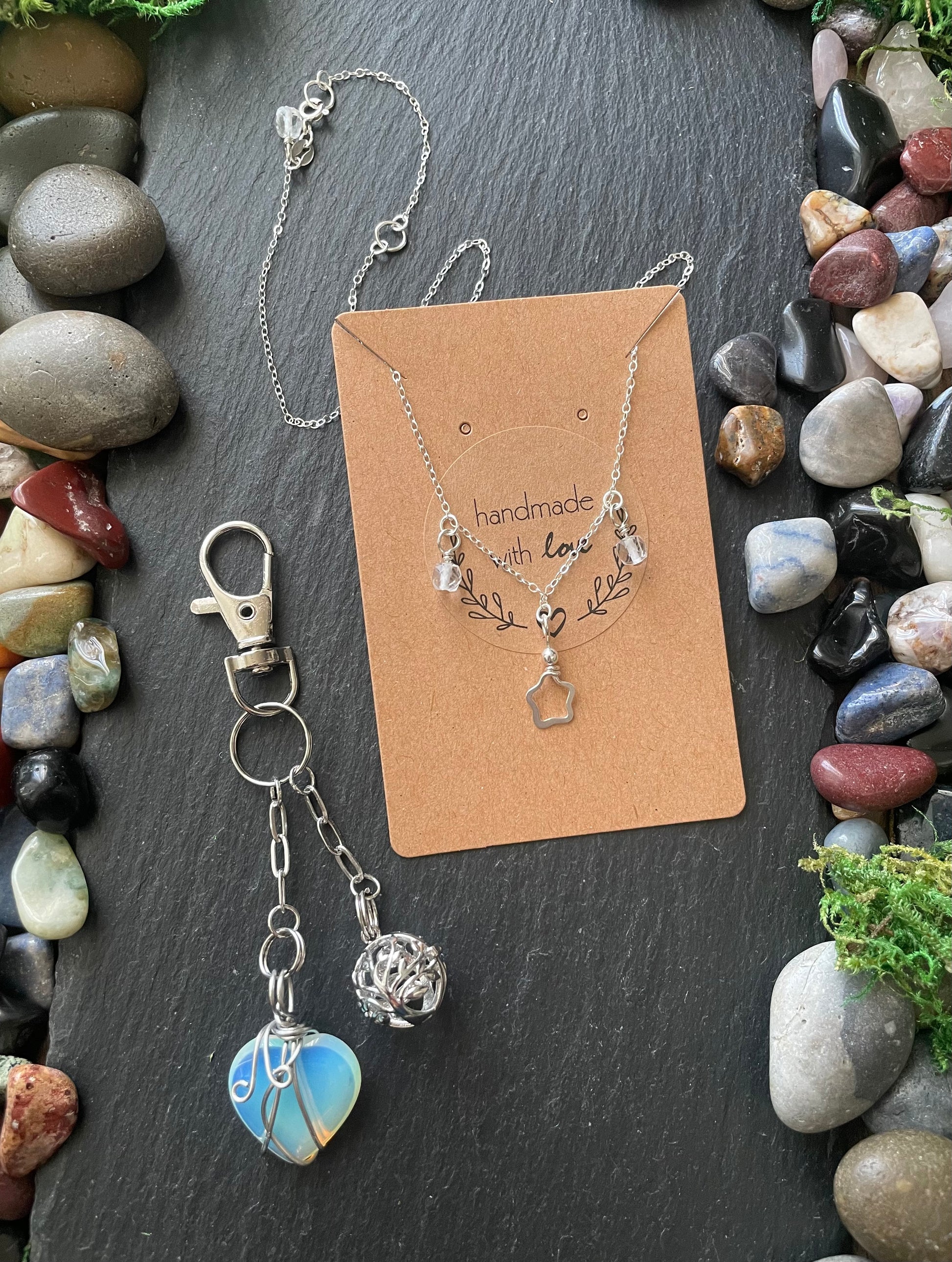 Jewelry set with necklace and keychain on a card, surrounded by stones and plants