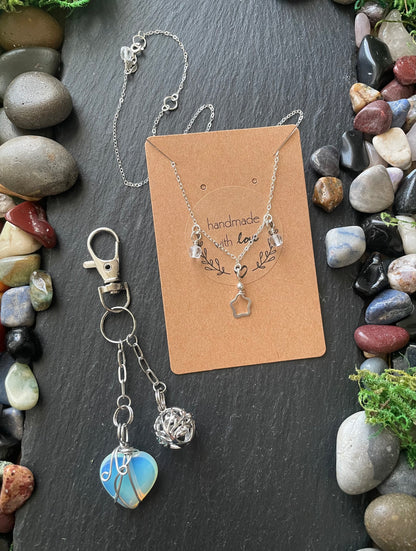 Jewelry set with necklace and keychain on a card, surrounded by stones and plants