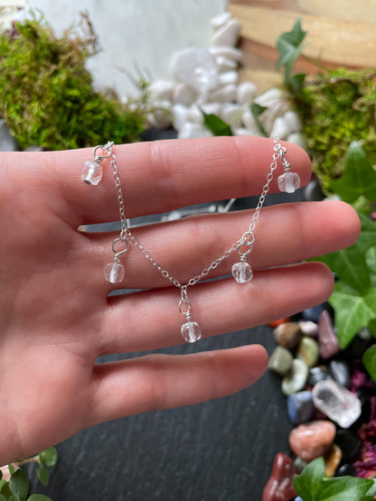 Hand holding a delicate silver necklace with clear beads against a natural background
