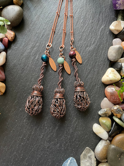 Copper necklaces with name tags on a dark surface with stones around
