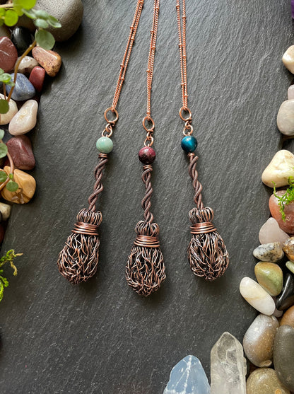 Three copper necklaces with intricate designs on a dark surface with stones and plants.