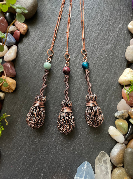 Three copper necklaces with intricate designs on a dark surface with stones and plants.