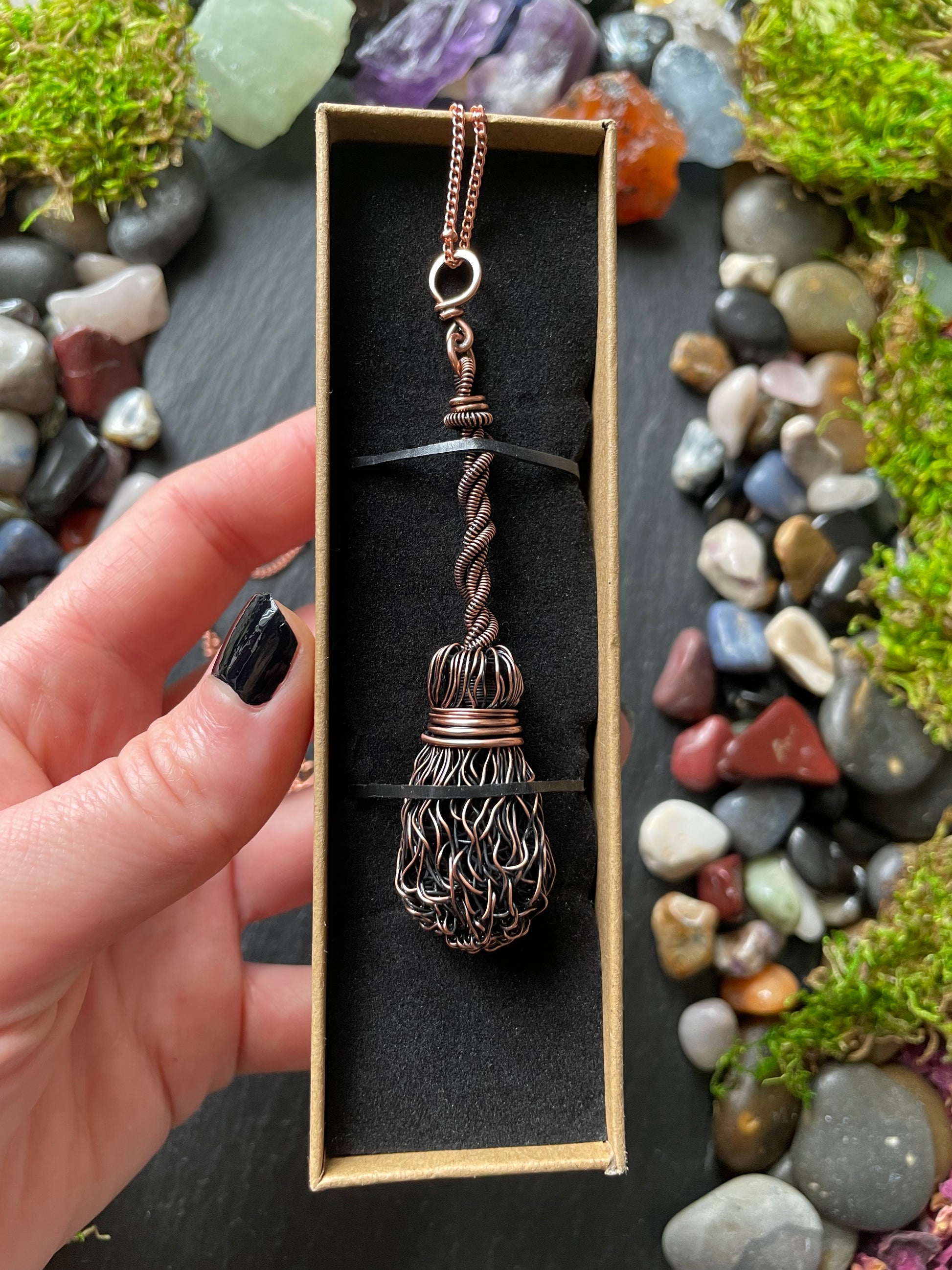 Hand holding a decorative necklace in a box with a natural stone background