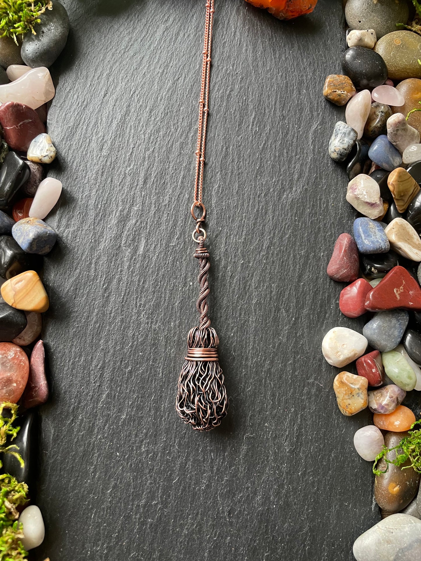 Copper necklace with a decorative pendant on a dark surface surrounded by multicolored stones.