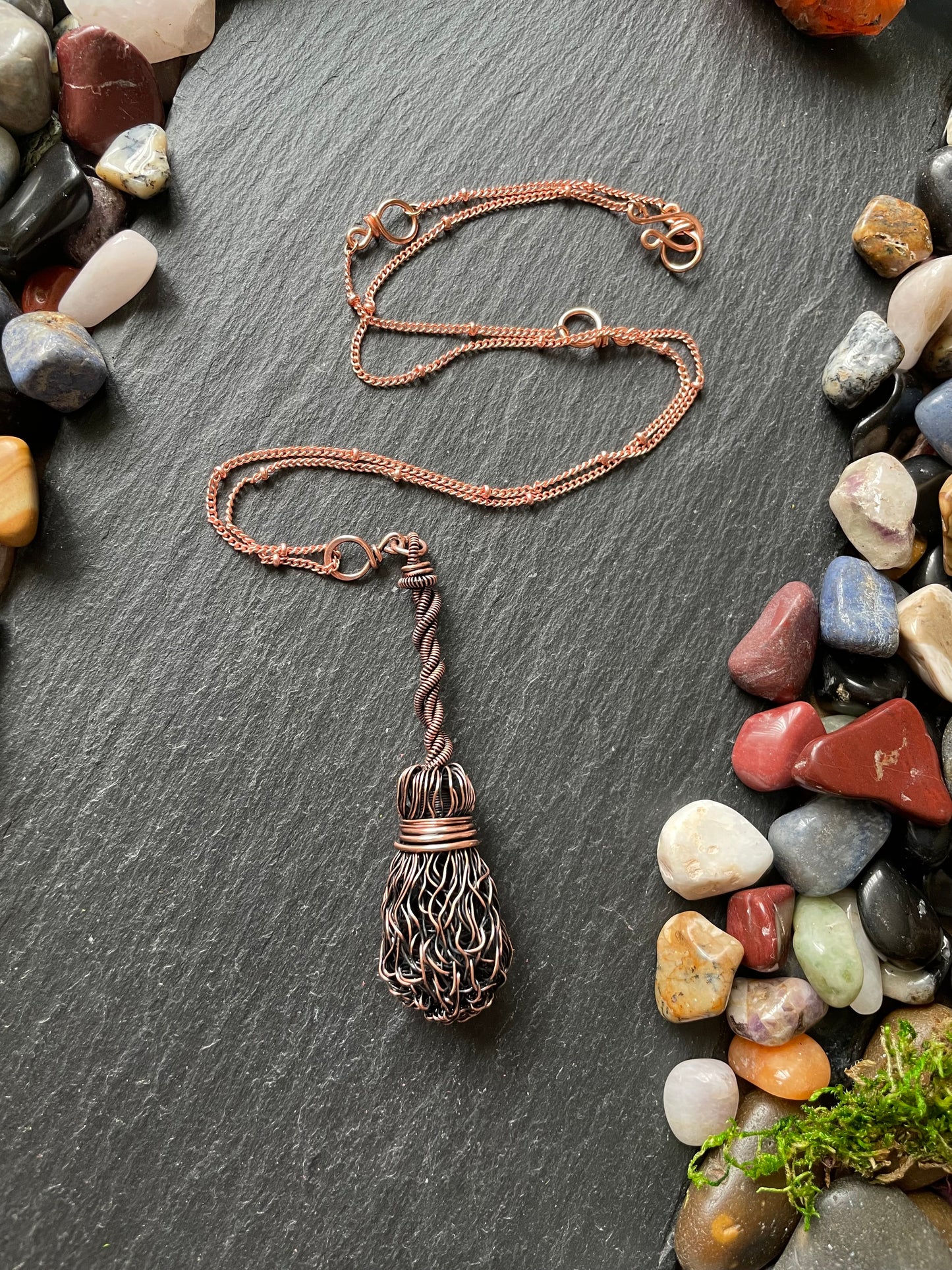 Copper necklace with a unique pendant on a dark surface with pebbles
