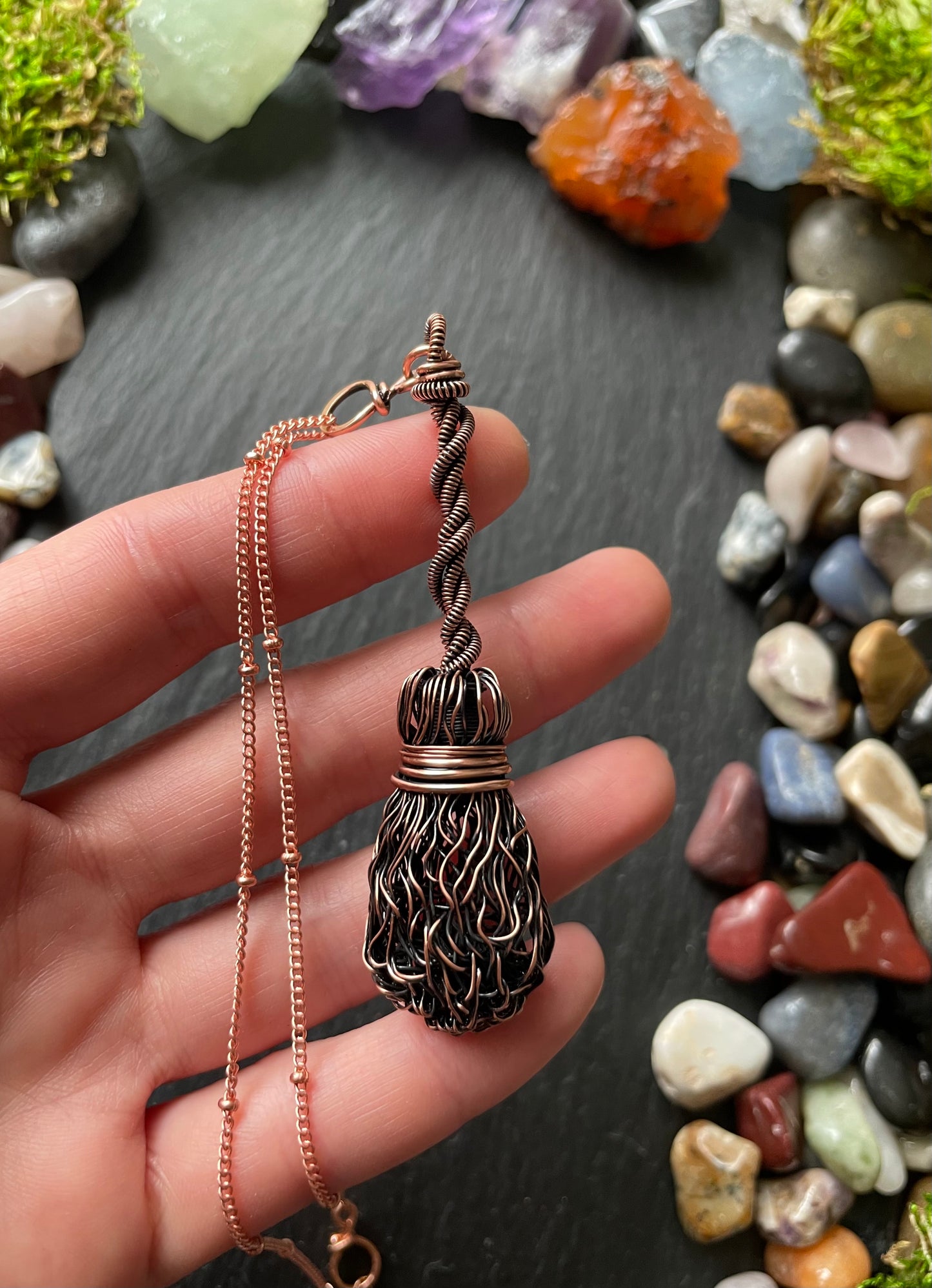 Hand holding a decorative necklace with a pendant against a background of multicolored stones.