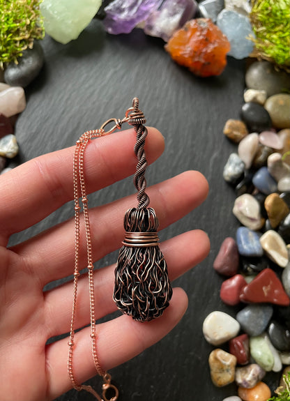Hand holding a decorative necklace with a pendant against a background of multicolored stones.