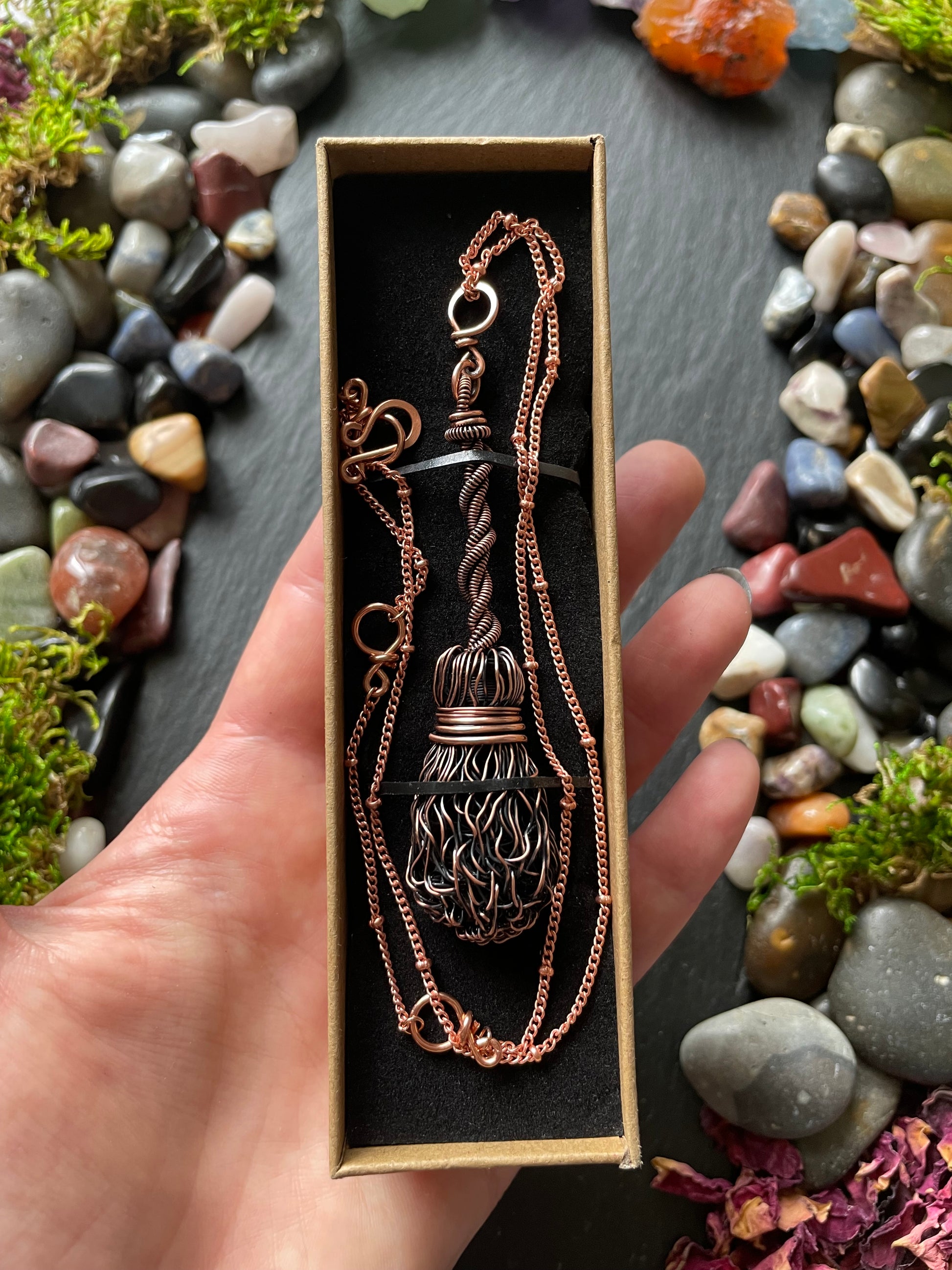 Hand holding a necklace with a decorative pendant against a natural stone background