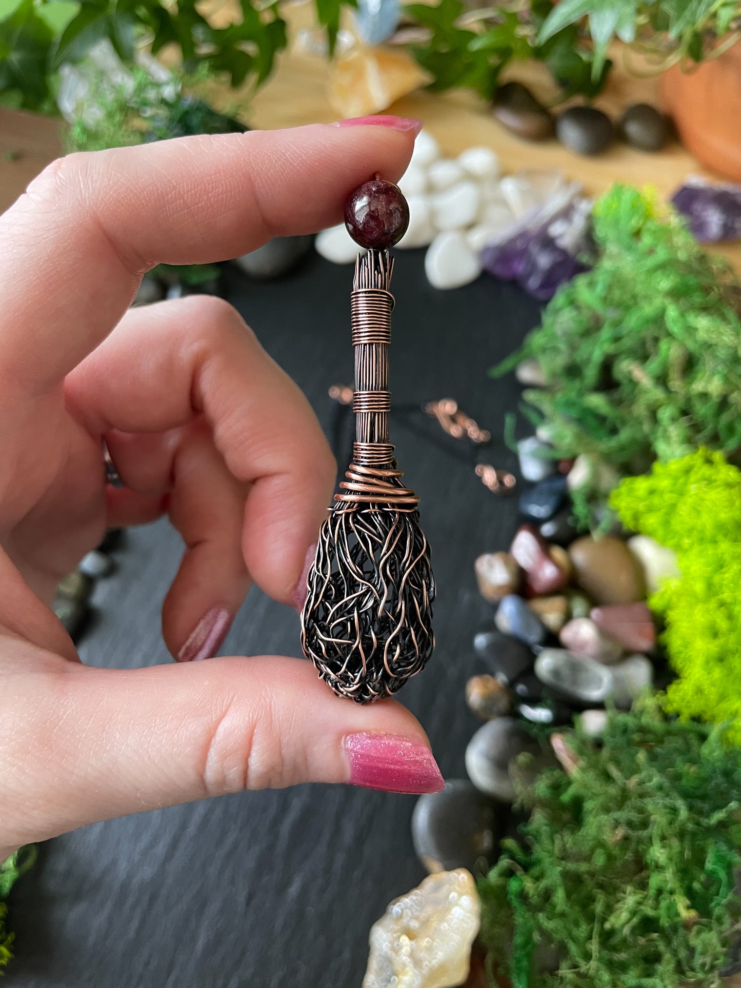 A miniature handmade copper broom held in hand with gemstones in background