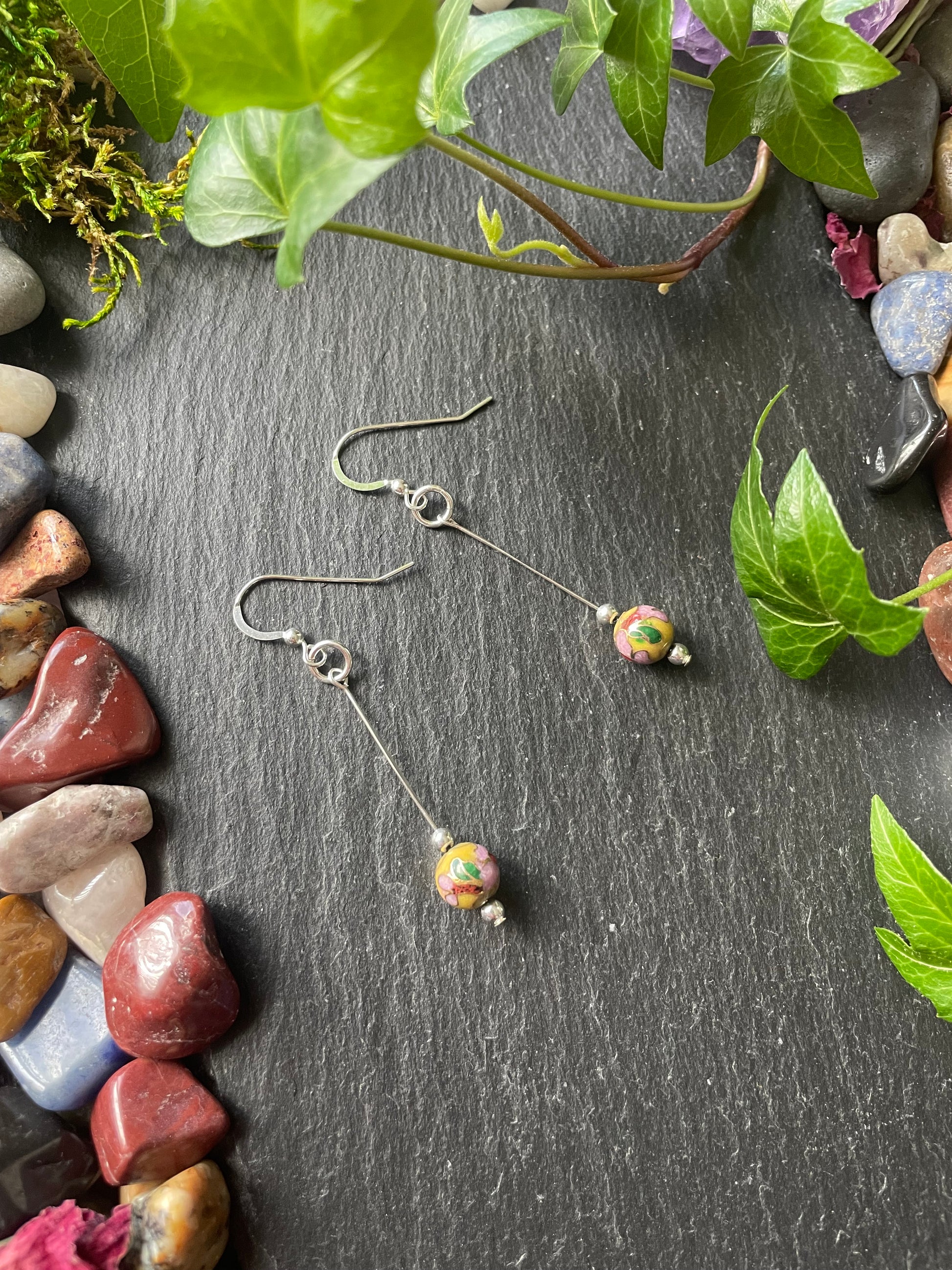 Earrings with yellow flower beads on a dark surface with stones and leaves