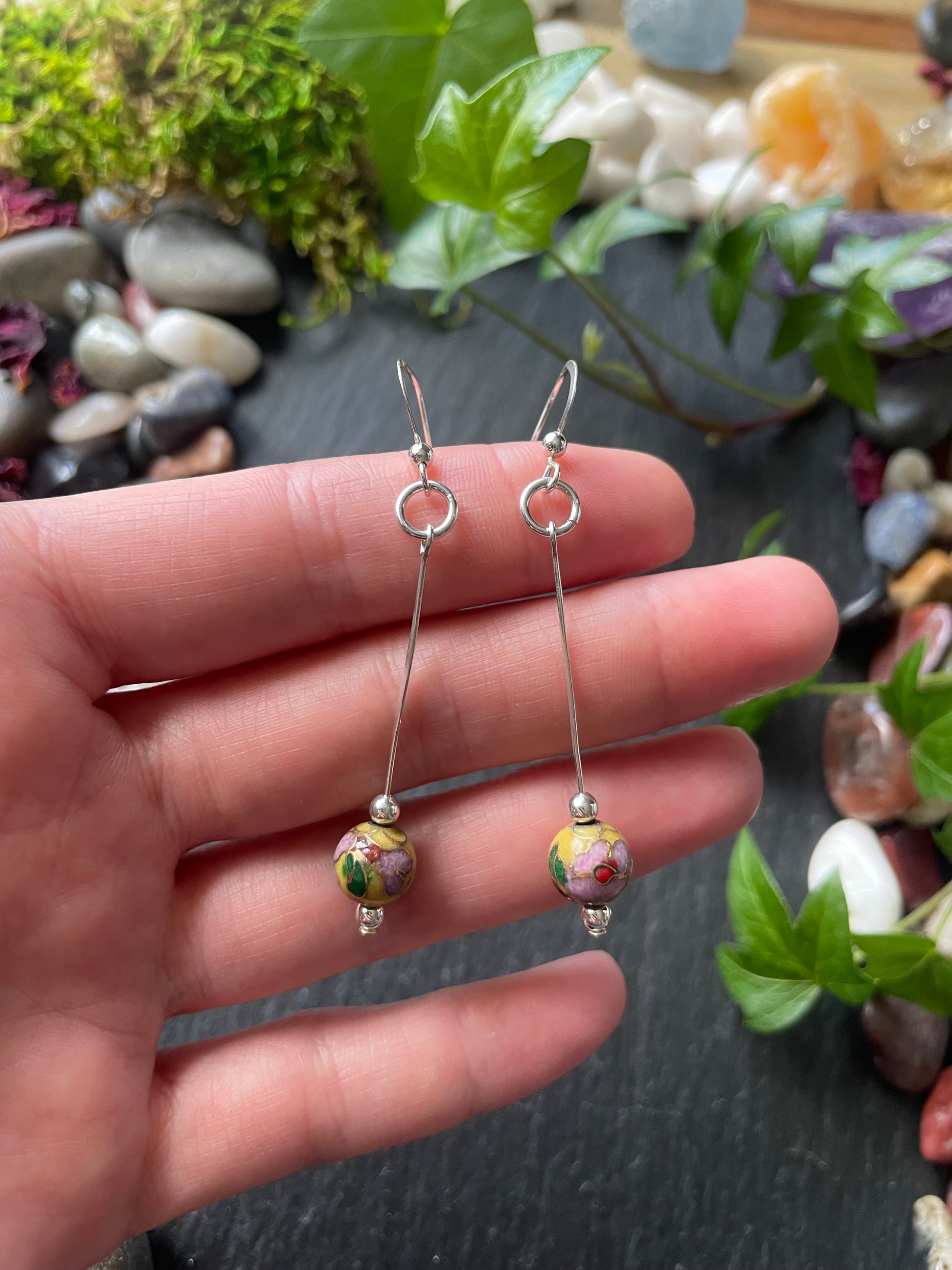 Silver earrings with beads held between fingers against a natural background.