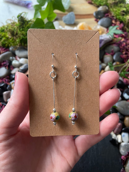Pair of earrings on a brown card held by a hand with a blurred natural background