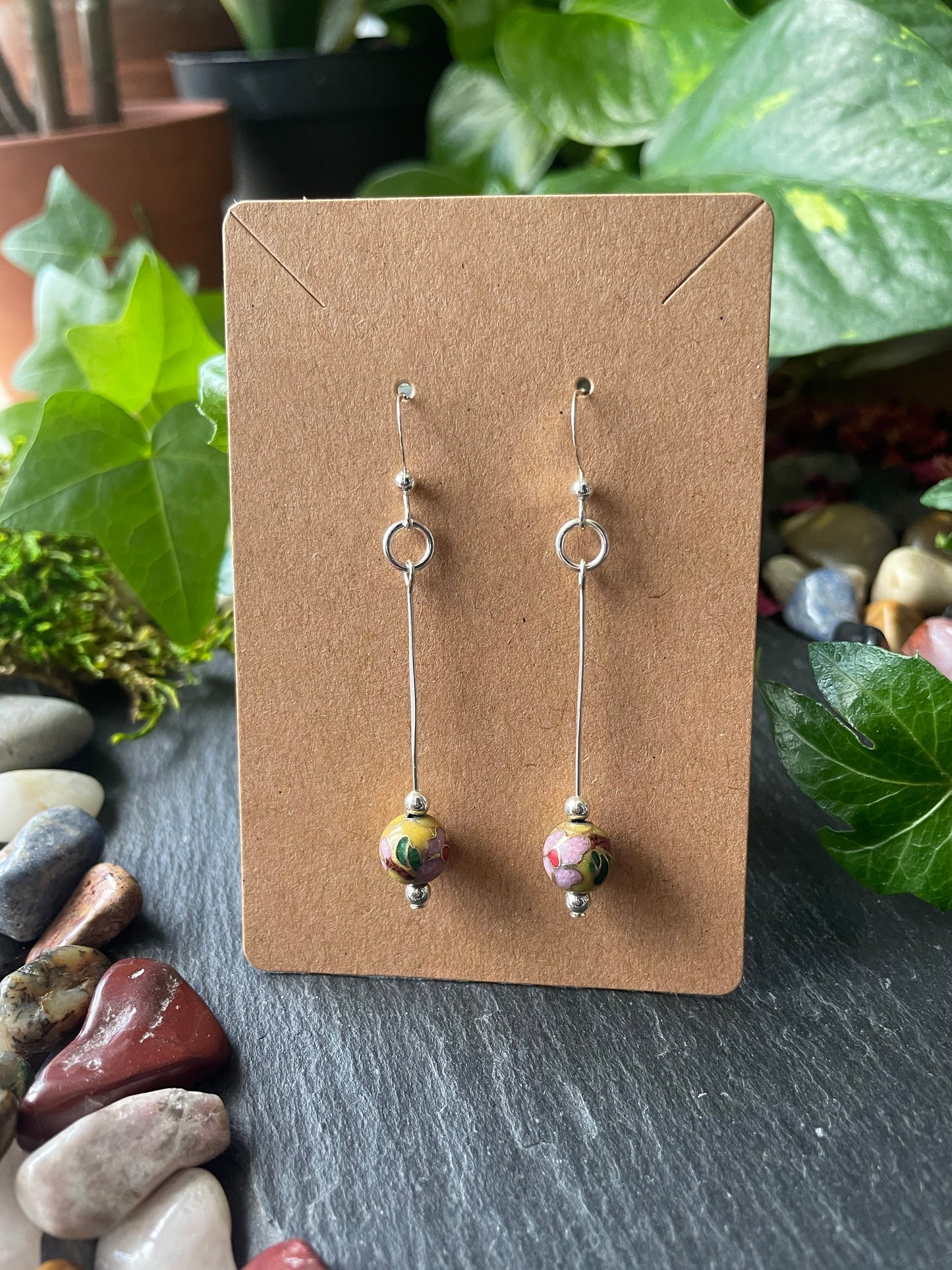 Two bead earrings on a cardboard backing with a natural stone and plant background.
