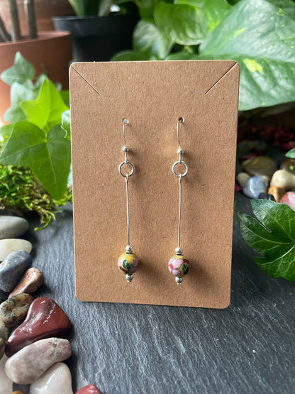 Two bead earrings on a cardboard backing with a natural stone and plant background.
