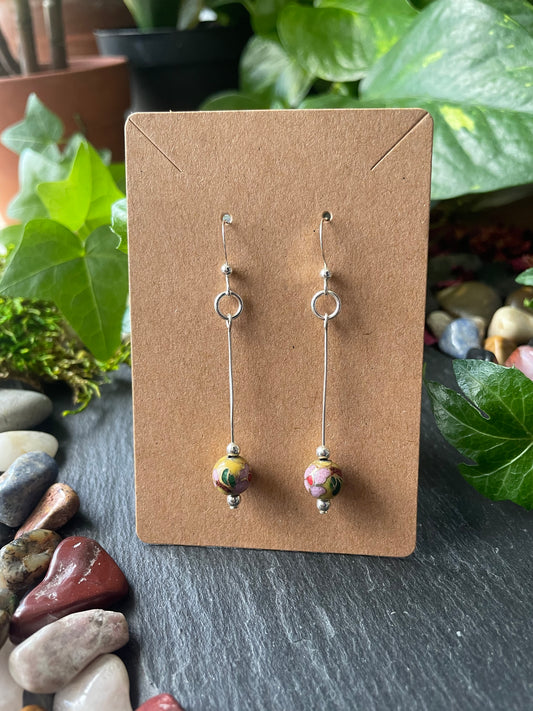Two bead earrings on a cardboard backing with a natural stone and plant background.