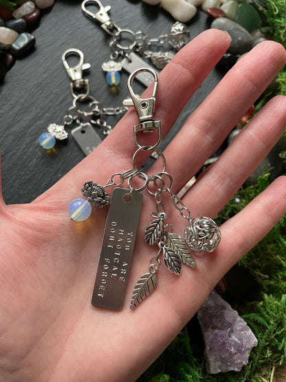 Hand holding a silver bag charm with engraved tag against a natural background